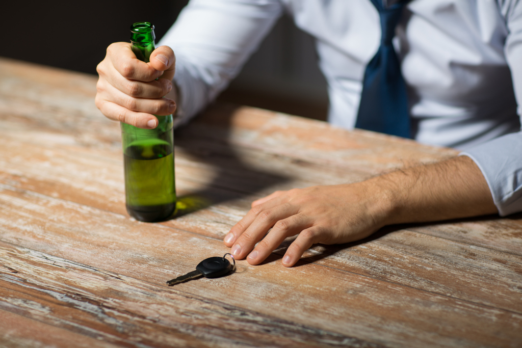 Hænder på et bord med bilnøgler og ølflaske